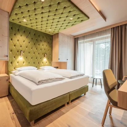 Modern hotel room with green upholstered bed, wood furnishings, and floor-to-ceiling window